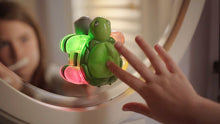 Load image into Gallery viewer, Reflection of child pressing green rubber button on turtle-shaped toothbrush timer stuck on bathroom mirror with white wood frame