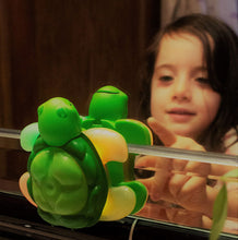 Load image into Gallery viewer, reflection of girl reaching to press the green rubber button on toothbrushing timer a turtle with flippers lit up.