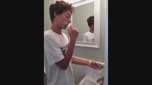 teenage boy brushes teeth holding and looking at the original two minute turtle timer 