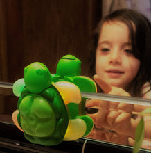Load image into Gallery viewer, reflection of girl reaching to press the green rubber button on toothbrushing timer a turtle with flippers lit up.
